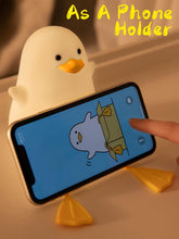 Yellow duck-shaped phone holder with a smartphone displaying an animated character on a beige surface.